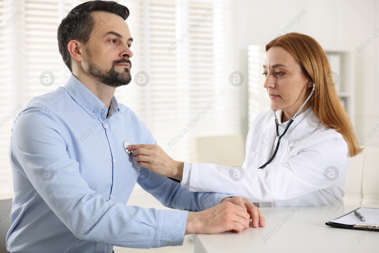 Photo of Cardiologist with stethoscope listening patient's heartbeat at desk in hospital