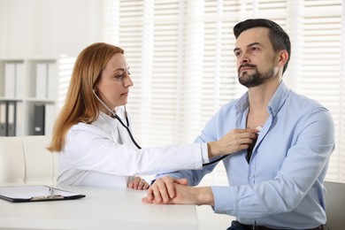 Cardiologist with stethoscope listening patient's heartbeat at desk in hospital