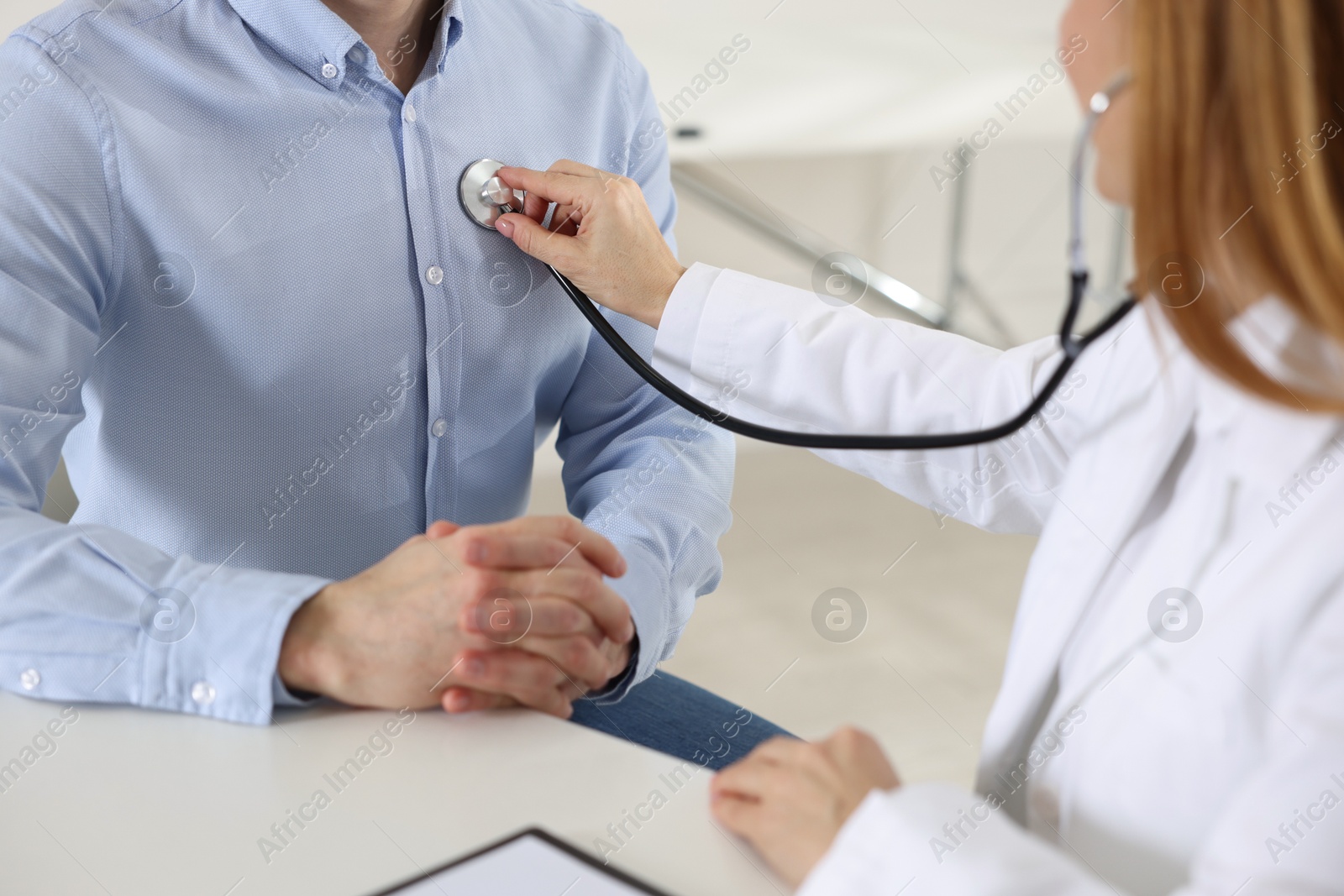 Photo of Cardiologist with stethoscope listening patient's heartbeat at desk in clinic, closeup