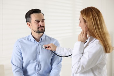 Photo of Cardiologist with stethoscope listening patient's heartbeat in clinic