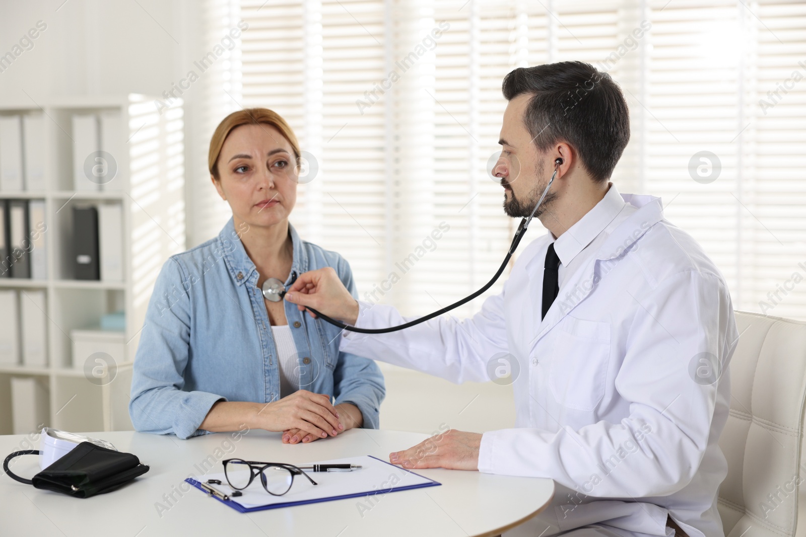 Photo of Cardiologist with stethoscope listening patient's heartbeat at desk in clinic