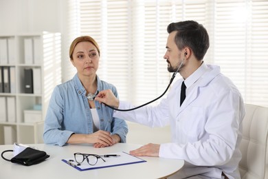 Photo of Cardiologist with stethoscope listening patient's heartbeat at desk in clinic