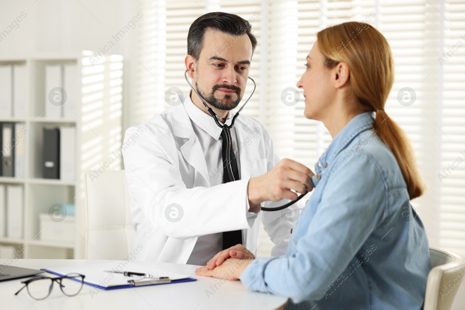 Photo of Cardiologist with stethoscope listening patient's heartbeat at desk in clinic