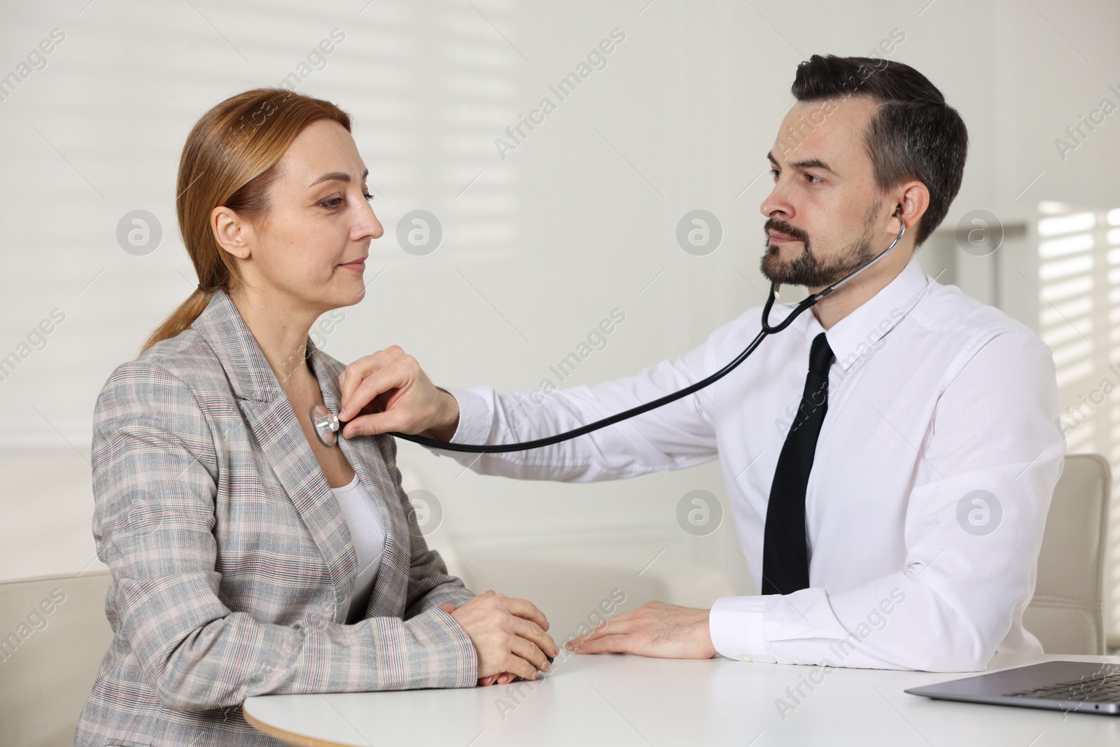 Photo of Cardiologist with stethoscope listening patient's heartbeat at desk in clinic