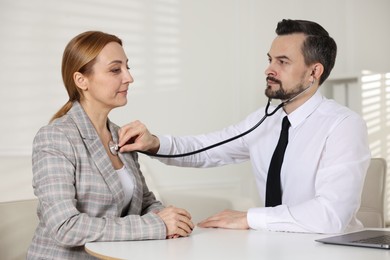 Cardiologist with stethoscope listening patient's heartbeat at desk in clinic