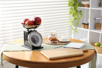 Photo of Retro mechanical kitchen scale, products and stationery on wooden table indoors