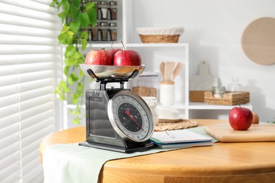 Photo of Retro mechanical kitchen scale, apples and stationery on wooden table indoors