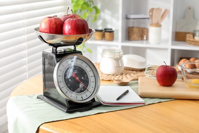 Photo of Retro mechanical kitchen scale, products and stationery on wooden table indoors