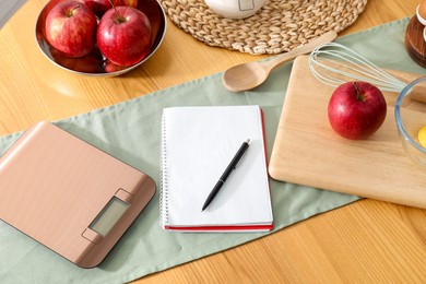 Photo of Electronic kitchen scale, apples and stationery on wooden table, above view