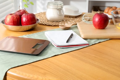 Photo of Electronic kitchen scale, products and stationery on wooden table indoors