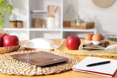 Electronic kitchen scale, products and stationery on wooden table indoors, closeup