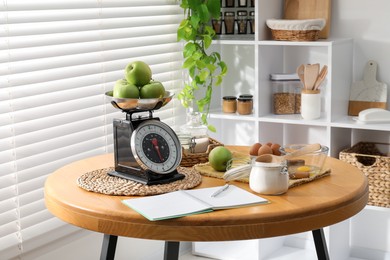 Retro mechanical kitchen scale, products and stationery on wooden table indoors