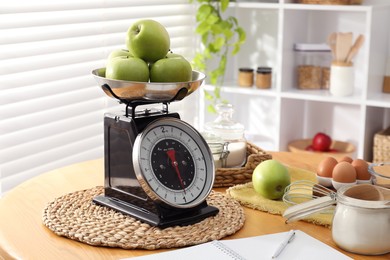 Retro mechanical kitchen scale, products and stationery on wooden table indoors