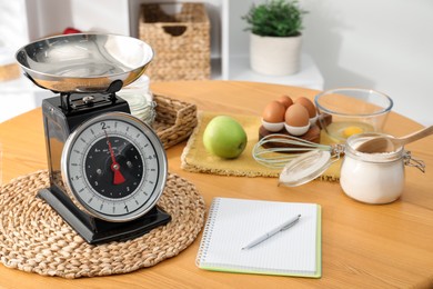 Photo of Retro mechanical kitchen scale, products and stationery on wooden table indoors