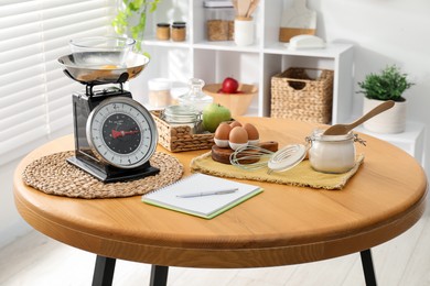 Photo of Retro mechanical kitchen scale, products and stationery on wooden table indoors