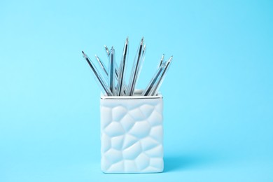 Photo of Many ballpoint pens in holder on light blue background