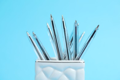 Photo of Many ballpoint pens in holder on light blue background, closeup