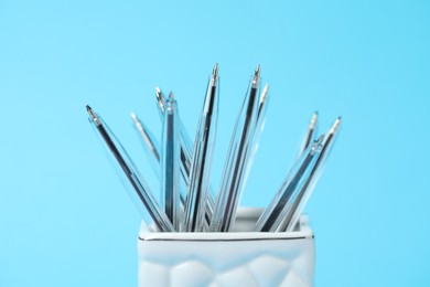 Photo of Many ballpoint pens in holder on light blue background, closeup