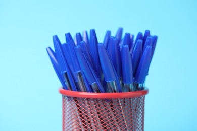 Photo of Many ballpoint pens in holder on light blue background, closeup