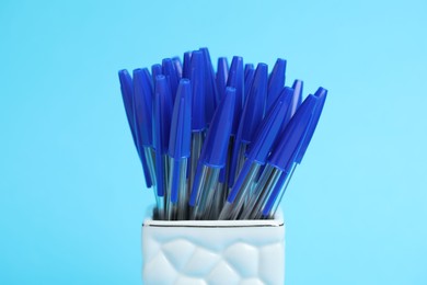 Photo of Many ballpoint pens in holder on light blue background, closeup