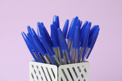 Photo of Many ballpoint pens in holder on pink background, closeup