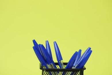 Photo of Many ballpoint pens in holder on green background, closeup