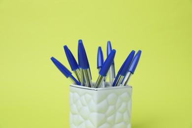 Photo of Many ballpoint pens in holder on green background, closeup