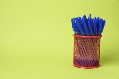 Photo of Many ballpoint pens in holder on green background, space for text