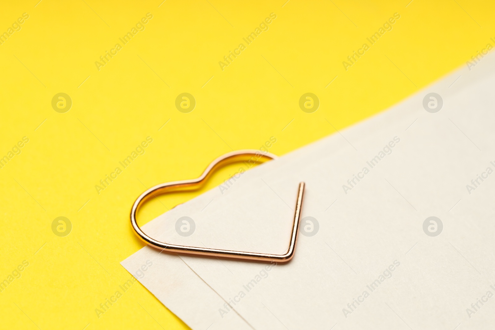 Photo of Heart shaped paper clip and notes on yellow background, closeup. Space for text