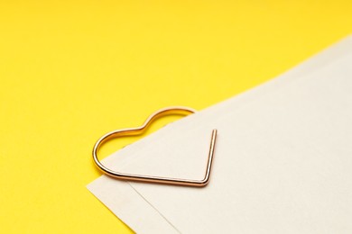 Photo of Heart shaped paper clip and notes on yellow background, closeup. Space for text