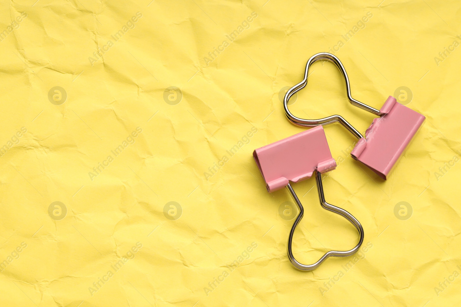 Photo of Beautiful binder clips on crumpled yellow paper, flat lay. Space for text