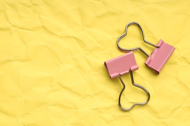 Beautiful binder clips on crumpled yellow paper, flat lay. Space for text