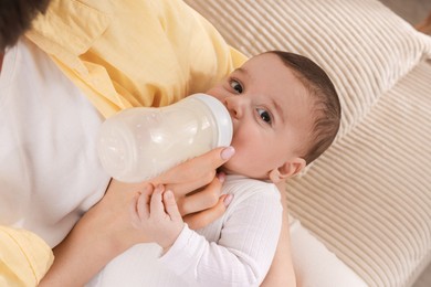 Photo of Mother feeding her little baby from bottle on sofa indoors, closeup