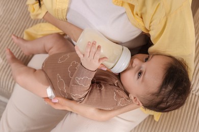 Photo of Mother feeding her little baby from bottle indoors, above view