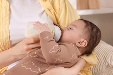 Photo of Mother feeding her little baby from bottle indoors, closeup