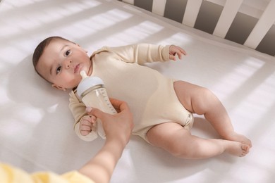 Photo of Mother feeding her little baby from bottle indoors, top view