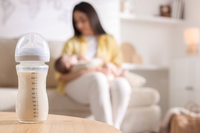 Photo of Mother holding her little baby indoors, focus on feeding bottle with milk