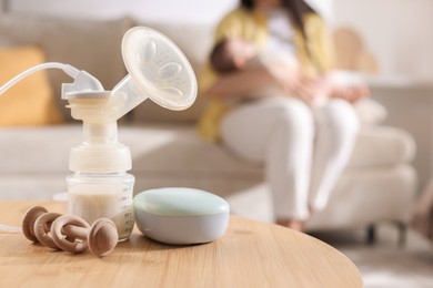 Photo of Mother holding her little baby indoors, focus on breast pump, teether and feeding bottle with milk