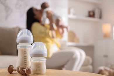 Photo of Mother holding her little baby indoors, focus on feeding bottles with milk and teether