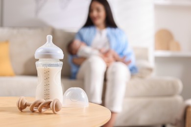 Photo of Mother holding her little baby indoors, focus on feeding bottle with milk and teether