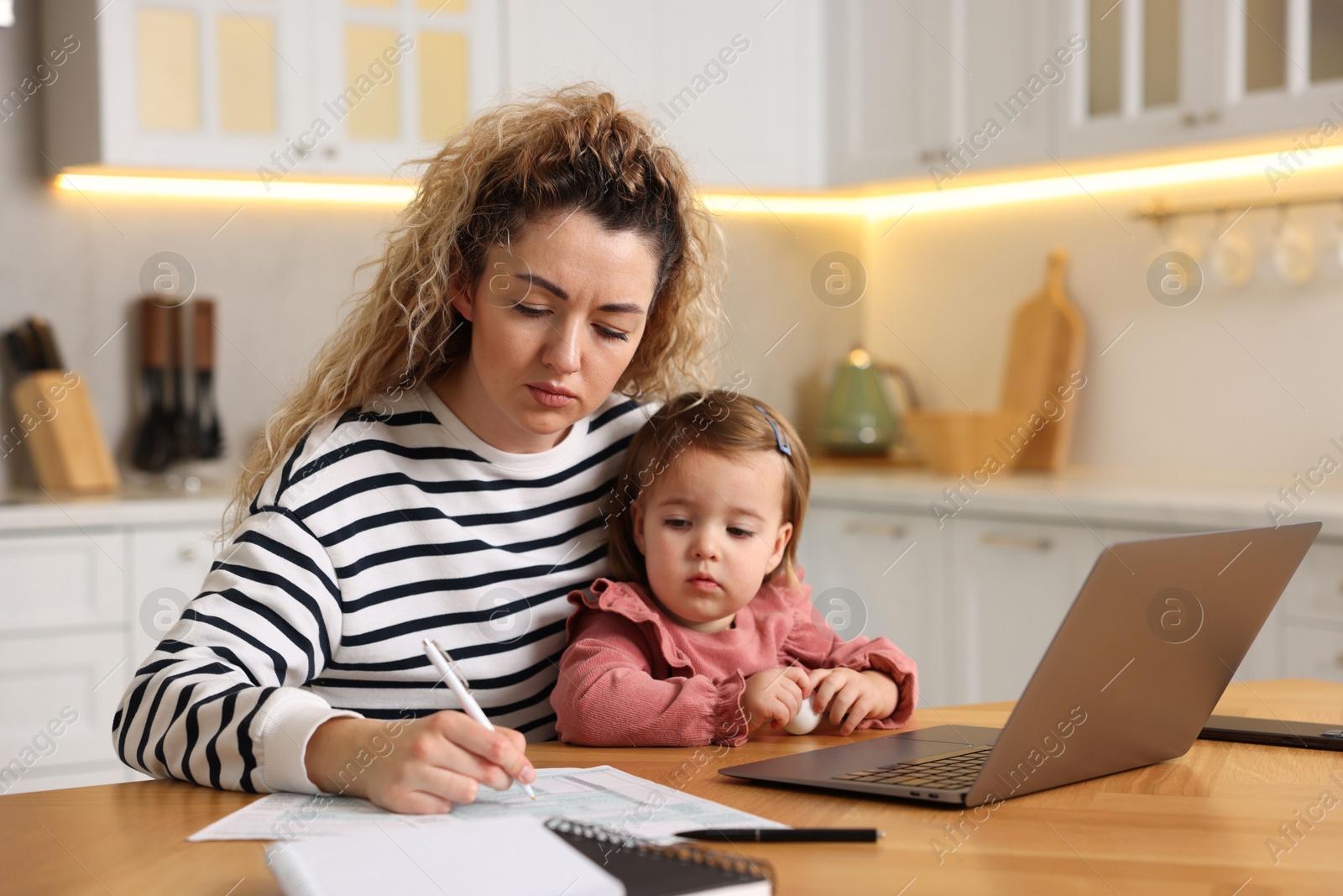 Photo of Single mother working and her daughter at wooden table in kitchen