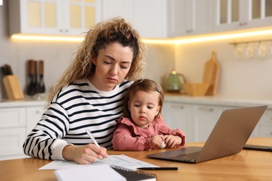 Single mother working and her daughter at wooden table in kitchen