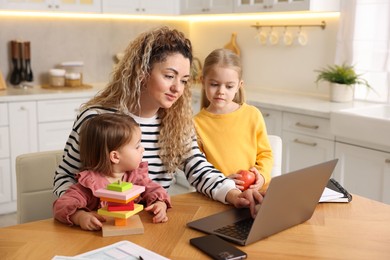 Photo of Single mother working on laptop and her daughters at table in kitchen