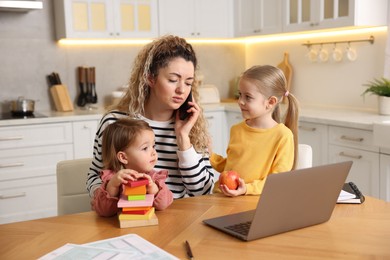 Photo of Single mother talking on smartphone and her daughters at table in kitchen