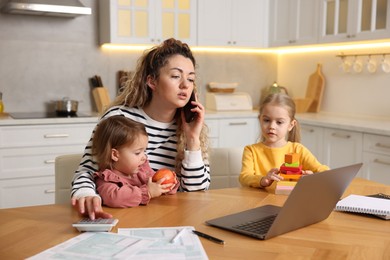 Photo of Single mother talking on smartphone and her daughters at table in kitchen