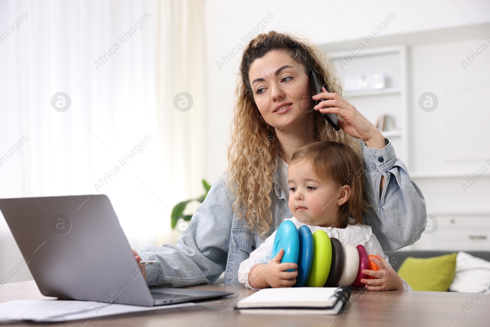 Photo of Work-family balance. Single mother talking on smartphone and her daughter playing at table indoors