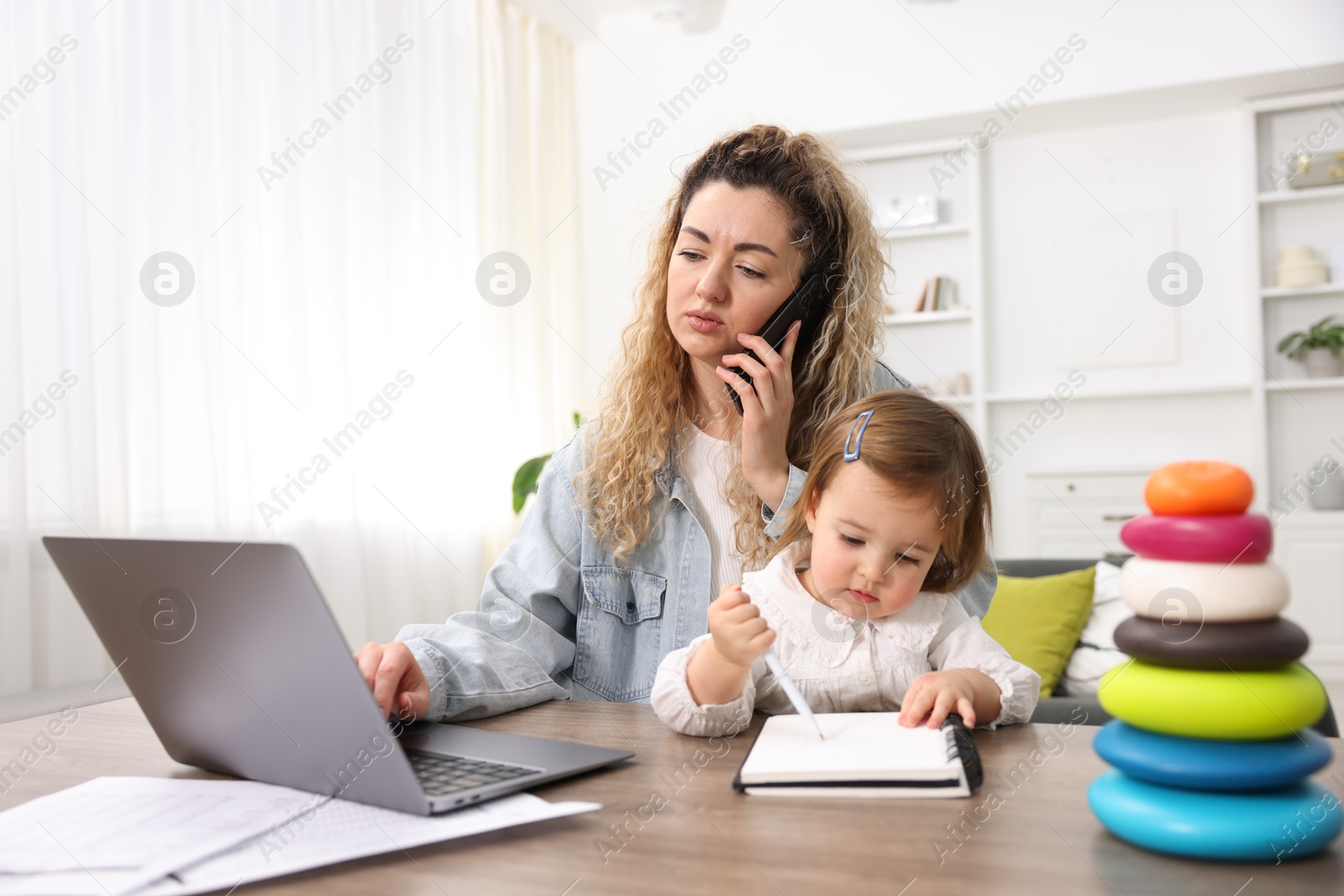 Photo of Work-family balance. Single mother talking on smartphone and her daughter at table indoors