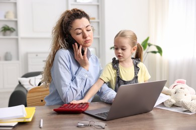 Photo of Work-family balance. Single mother talking on smartphone and her daughter at table indoors