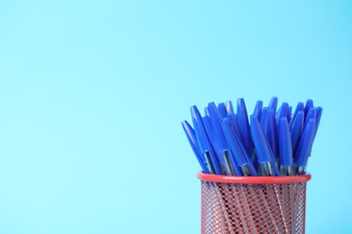 Photo of Many ballpoint pens in holder on light blue background, closeup. Space for text