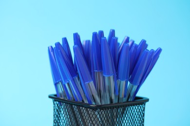 Photo of Many ballpoint pens in holder on light blue background, closeup